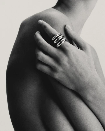 Close-up portrait of a person wearing three stacked silver rings on a finger resting against their bare shoulder.