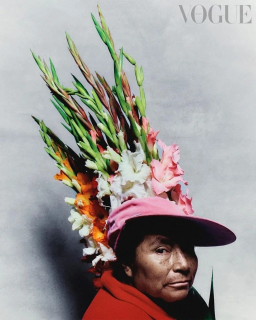 Portrait of a woman in a pink hat adorned with colorful gladiolus flowers against a light gray background with Vogue logo.