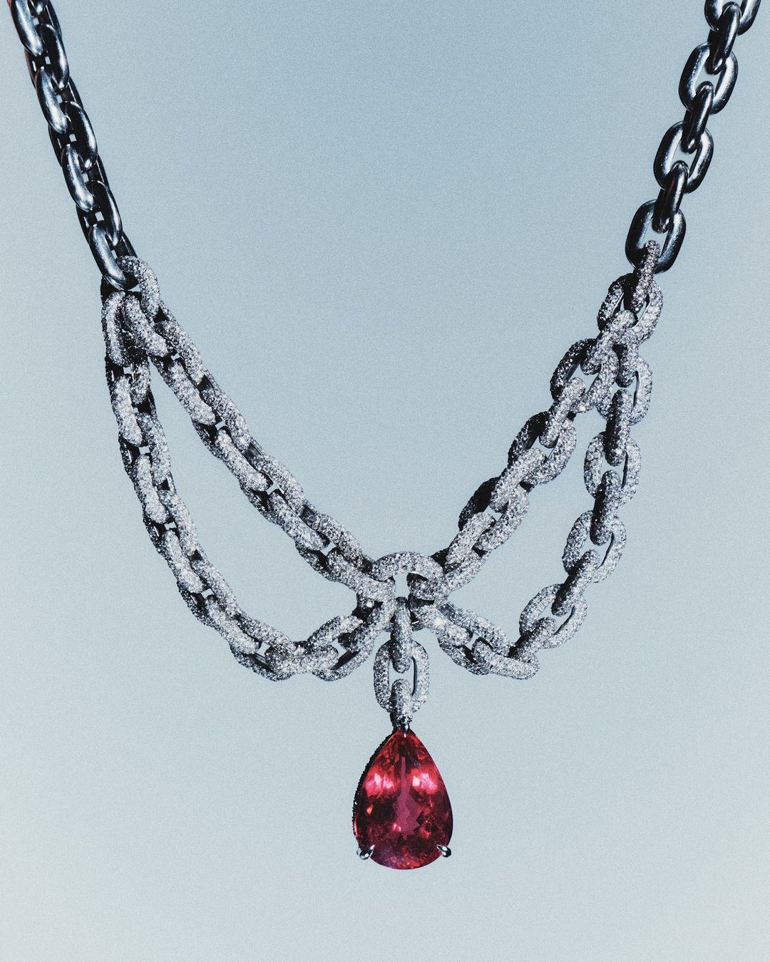 Elegant jewelry shot of a diamond encrusted, silver chain necklace with a large, tear-drop shaped, pink tourmaline pendant.