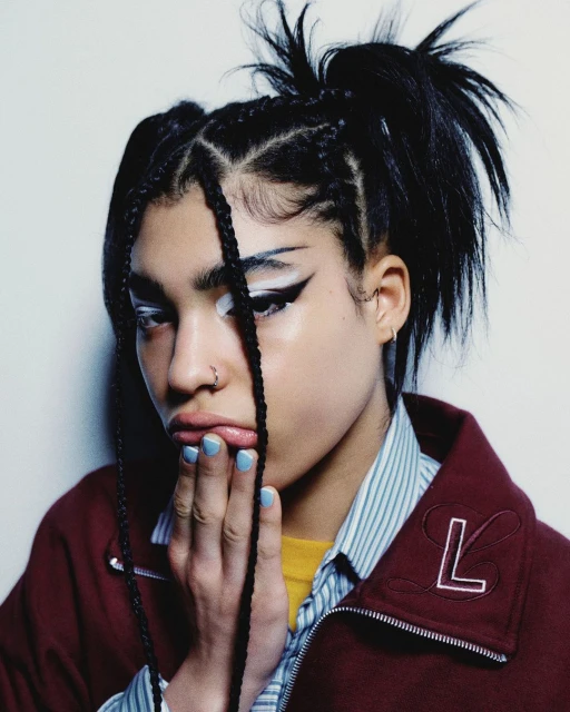 Close-up portrait of a young adult woman with dark braided hair in a high ponytail, wearing dramatic white and black eye makeup.