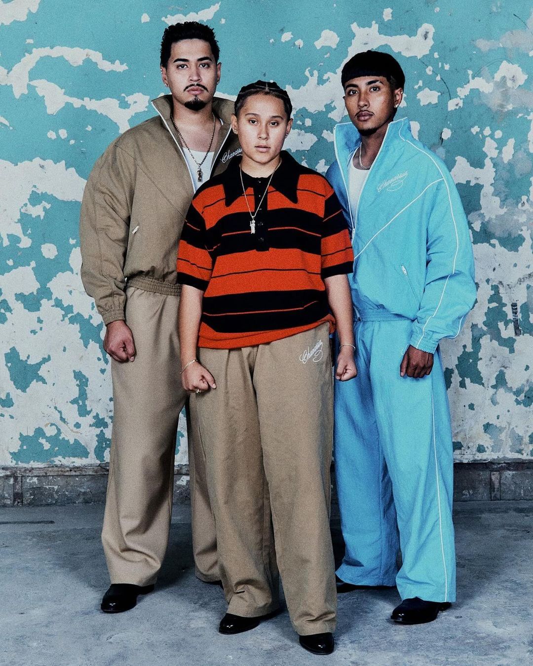 Three people posing in front of textured wall. Adult male and female in striped shirt and matching pants and tracksuits, indoor setting.