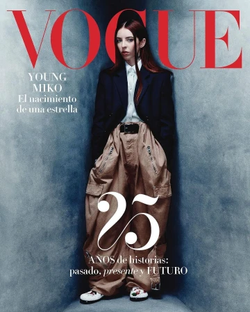Magazine cover portrait featuring a woman wearing an oversized blazer and baggy cargo trousers standing against a textured blue wall.