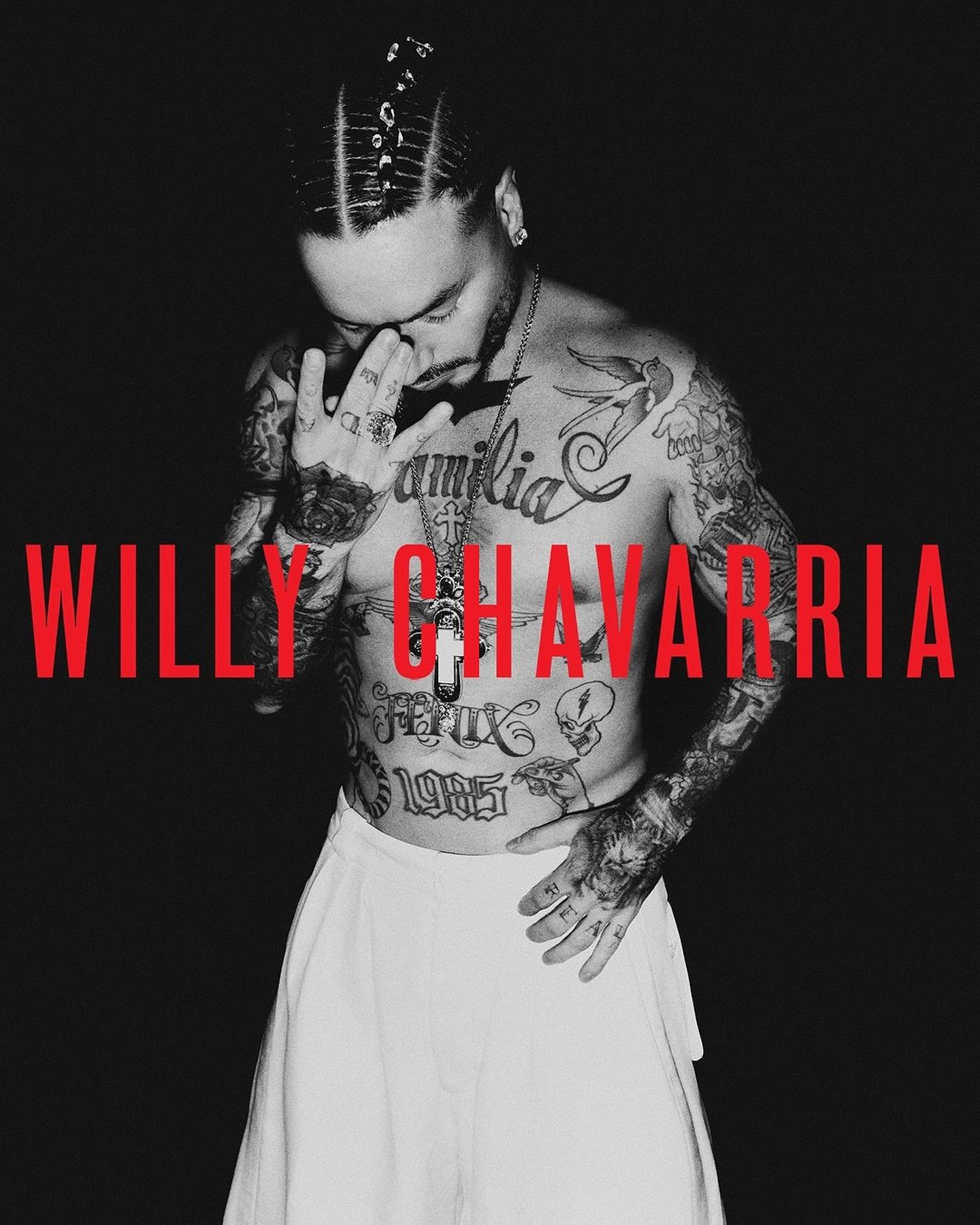 Monochrome portrait of a shirtless tattooed man wearing white trousers with bold red typography across his chest.