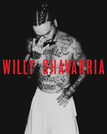 Monochrome portrait of a shirtless tattooed man wearing white trousers with bold red typography across his chest.