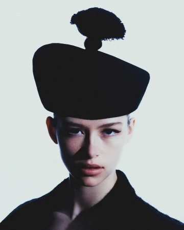 Close-up portrait of a model wearing a dark structured hat with a pom-pom by photographer Diego Bendezu