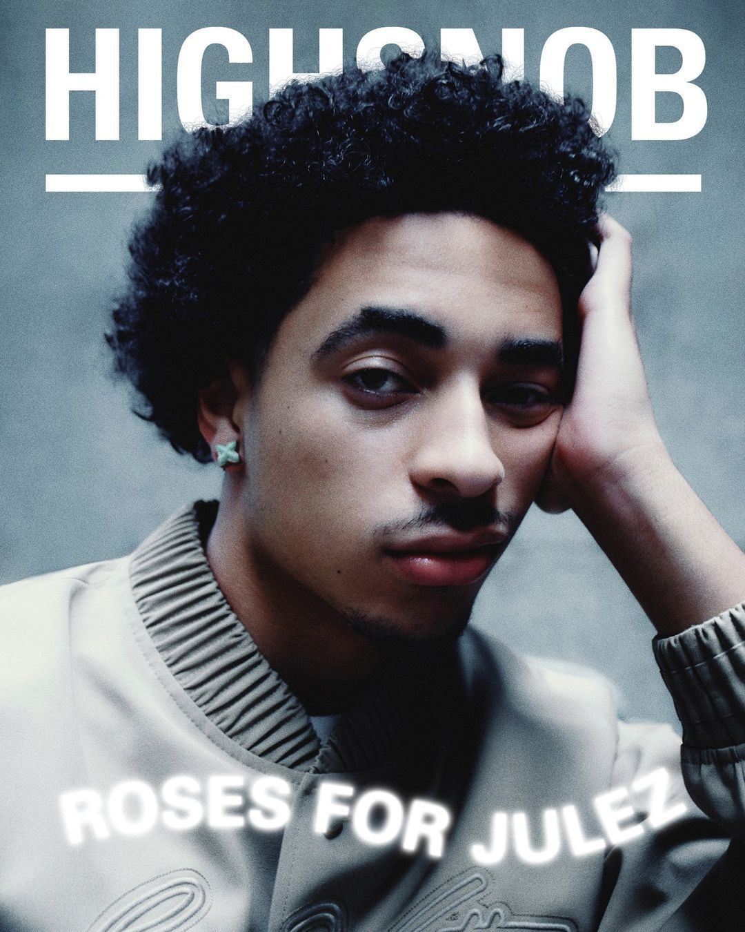 Portrait of a young man with curly hair wearing a beige jacket against a textured grey background by Diego Bendezu