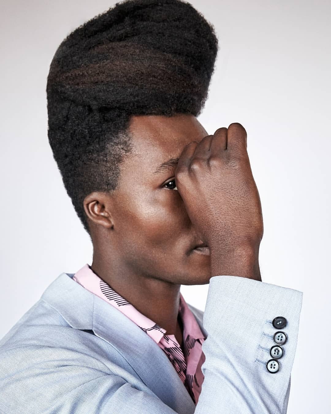 Close-up of an African American male model with a high-top fade wearing a light blue blazer and pink shirt against a neutral backdrop.