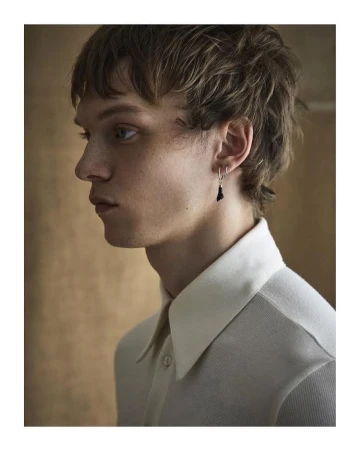 Profile portrait of a young man wearing a white collared shirt and silver earrings photographed in London