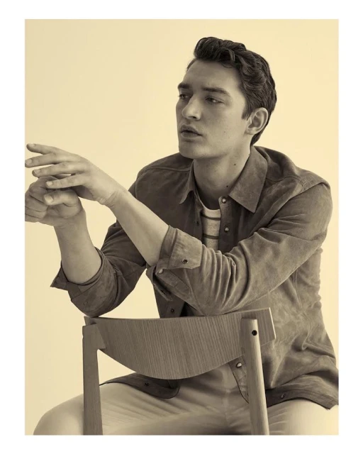 Portrait of a young man in a collared shirt, seated in a chair and looking off to the side, captured in a photo studio setting.