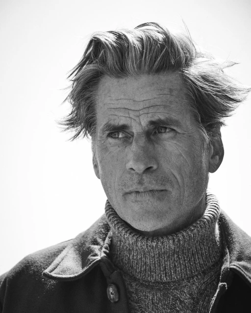 Black and white portrait of a mature adult male in a textured sweater and jacket looking away from the camera with a serious expression.