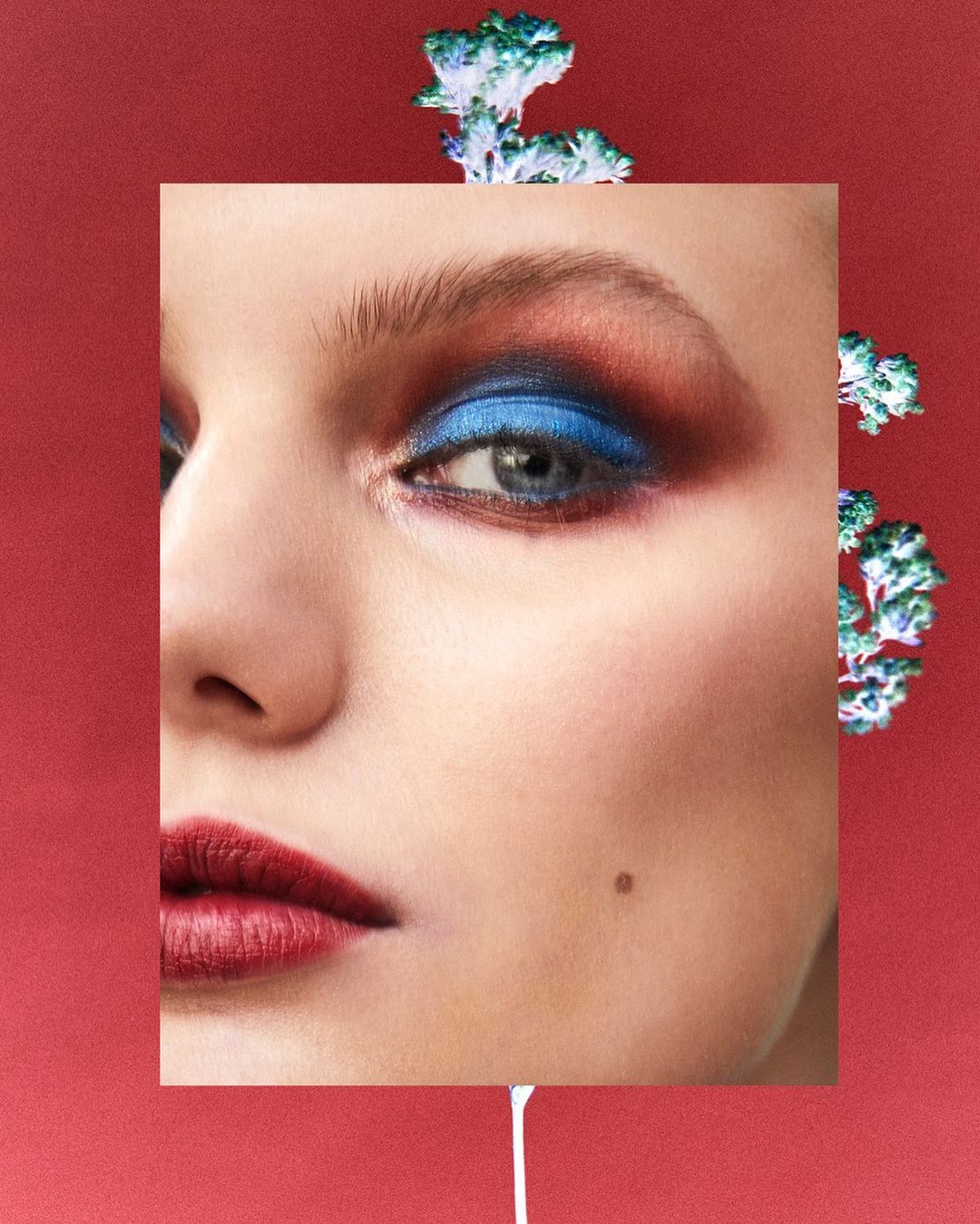 Close-up of a woman's face with bold eye makeup featuring blue and burgundy eyeshadow. Image framed with a red border and liquid accents.