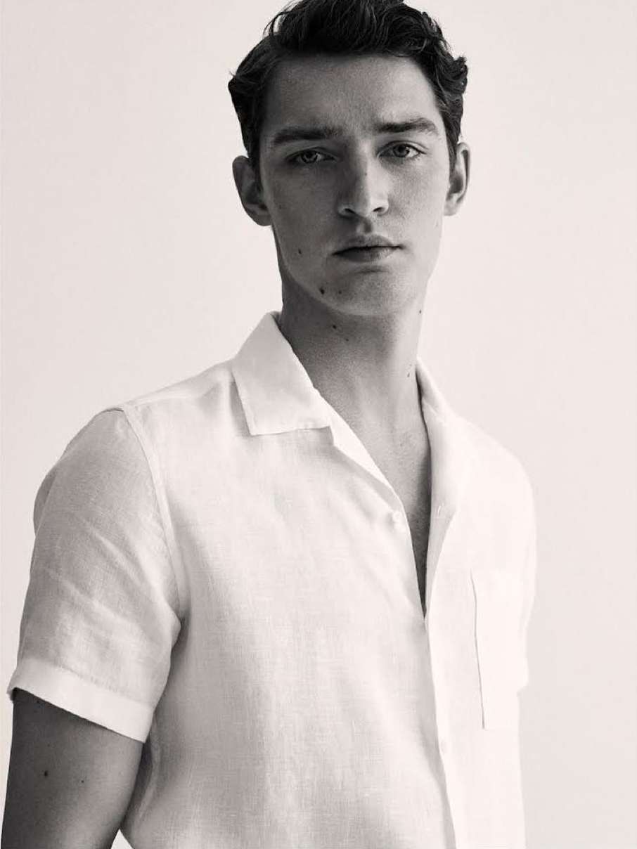 Monochrome portrait of a young adult male with dark hair, wearing a white linen shirt, looking directly at the camera, studio lit.