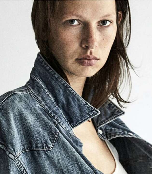 Close-up portrait of a woman wearing a distressed denim jacket against a neutral white background by Diego Merino