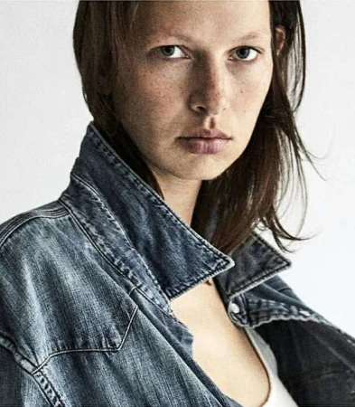 Close-up portrait of a woman wearing a distressed denim jacket against a neutral white background by Diego Merino