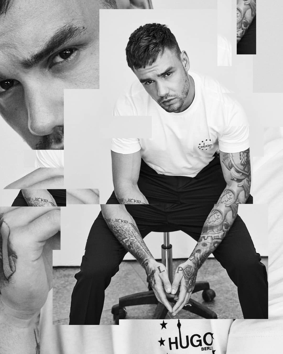 Monochrome studio portrait of a fair-skinned man with short hair, tattoos, and casual white t-shirt seated in front of a white background.