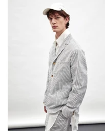 A male model wearing a striped seersucker blazer and white cap against a plain white studio backdrop.