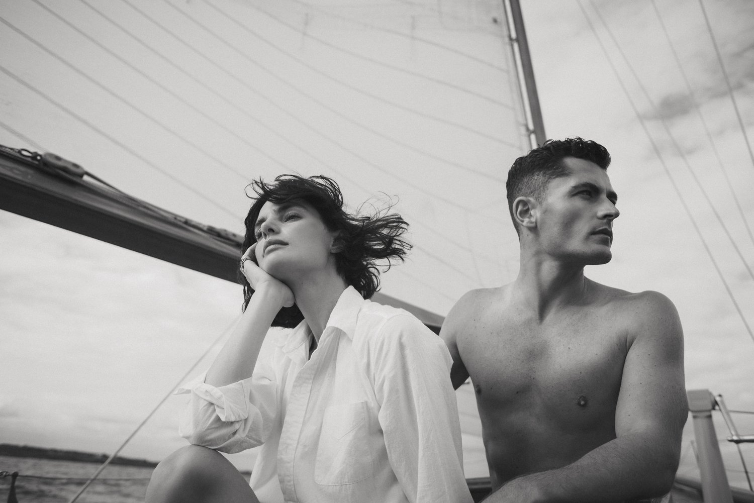 Monochrome portrait of a man and woman on a sailboat with sail and cloudy sky as background; medium shot, lifestyle photography.
