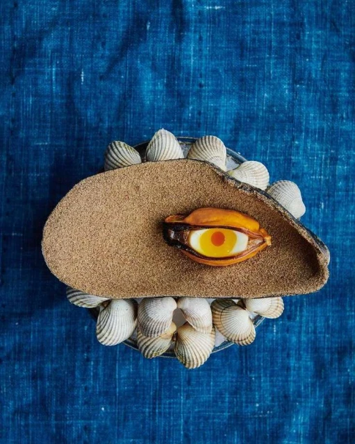 Overhead shot of food art featuring seafood and decorative shells on a blue surface, showcasing culinary creativity.