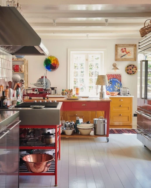 Bright kitchen interior with red and yellow cabinets, stainless steel appliances, white walls, and a hardwood floor.