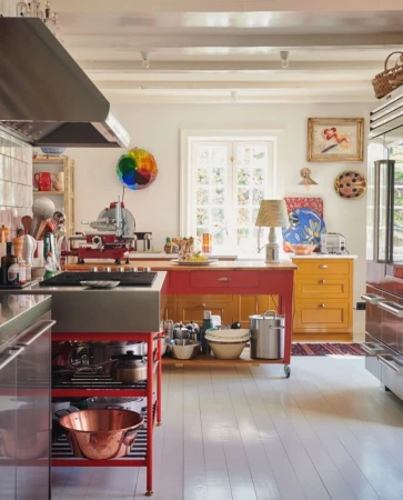 Bright kitchen interior with red and yellow cabinets, stainless steel appliances, white walls, and a hardwood floor.