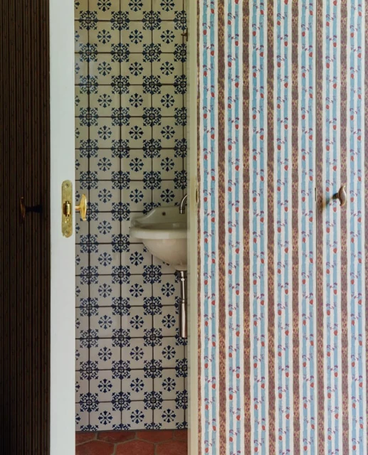 Bathroom interior showcasing patterned tile walls, a small sink, and an open doorway, creating a vintage and decorative atmosphere.