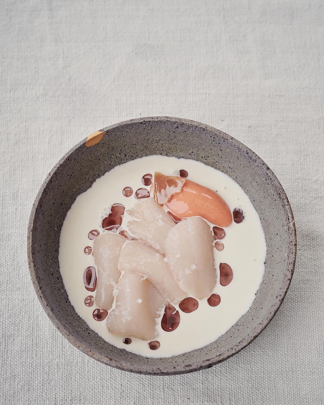 Overhead shot of a grey bowl filled with white liquid, white pieces, and orange sauce, set on a textured white background.