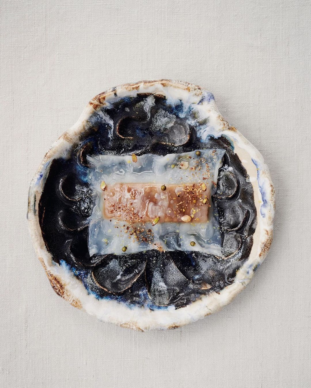 Overhead shot of food dish with glaze on oyster-shaped plate. Main dish of meat rectangle on translucent gelatin.