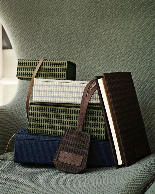 Stack of woven boxes and a book, featuring a patterned bookmark on a textured green chair, creating a cozy, textured indoor scene.