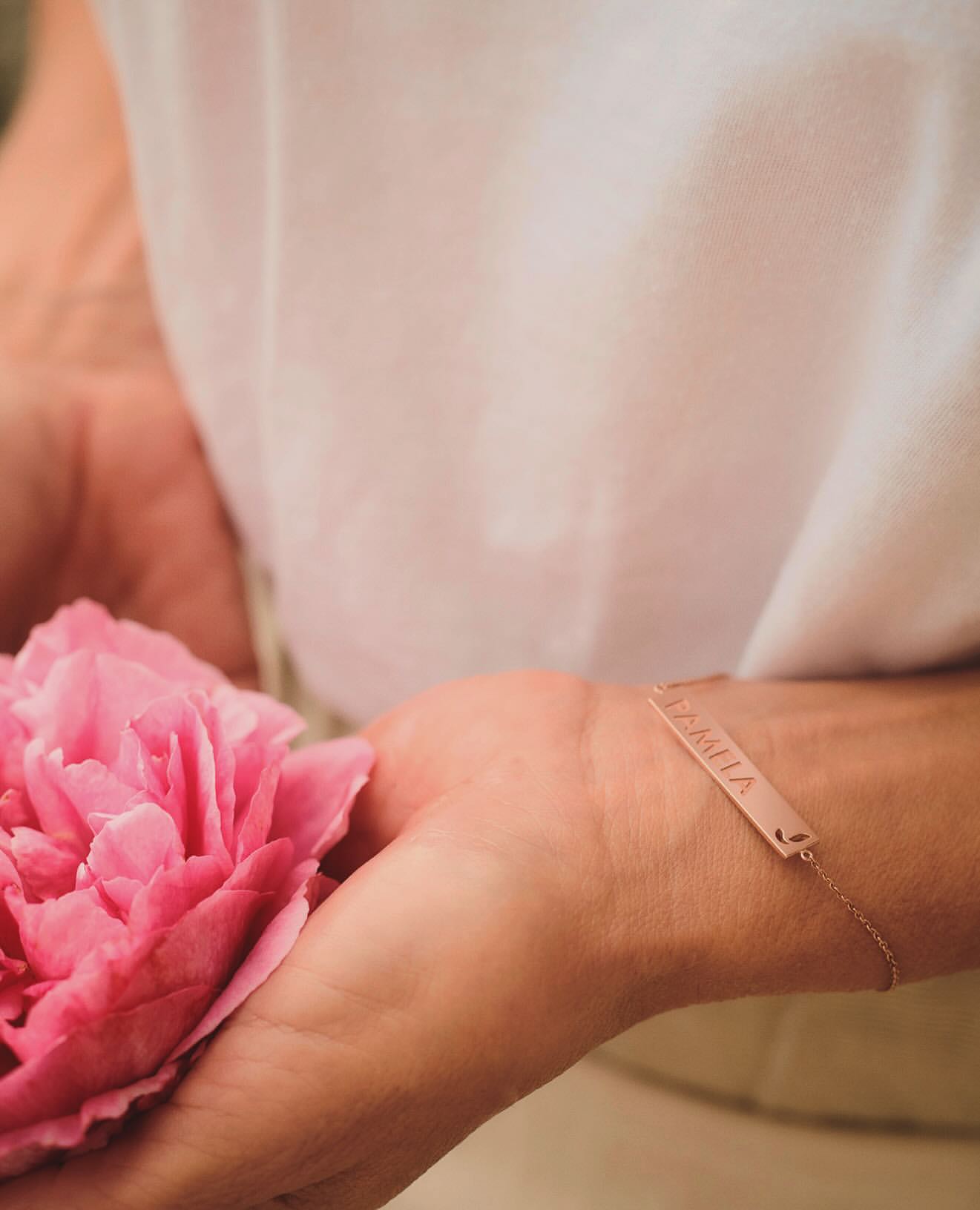 Close-up of hands holding a pink peony flower wearing a rose gold bar bracelet