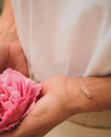 Close-up of hands holding a pink peony flower wearing a rose gold bar bracelet