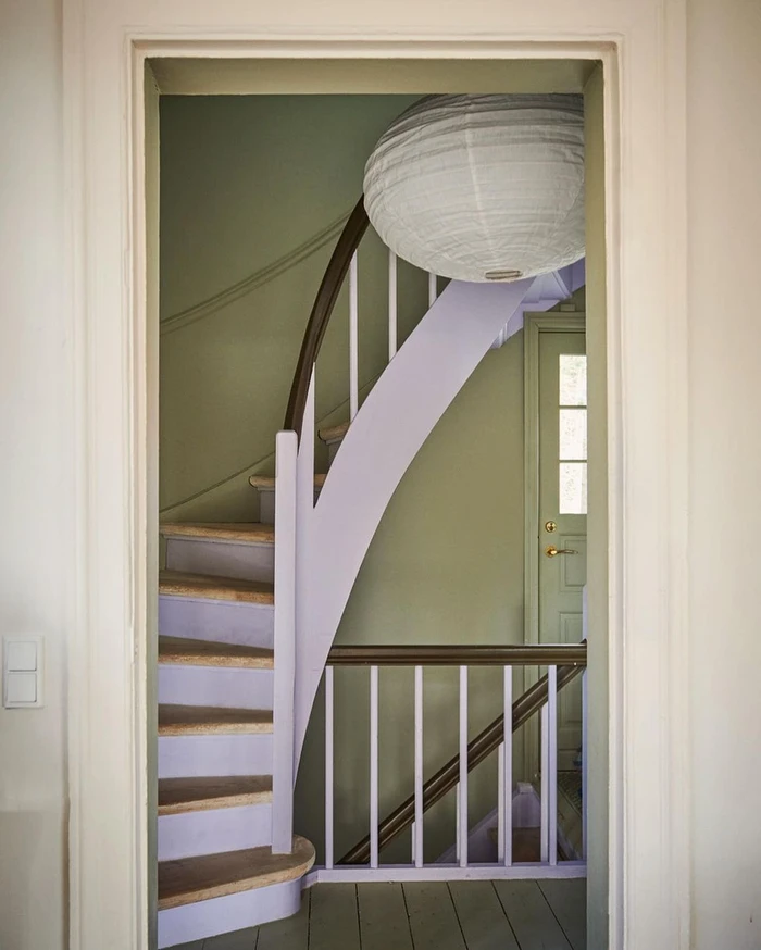 Interior view through a doorway showing a curved staircase with lavender risers and a large round paper lantern hanging above.