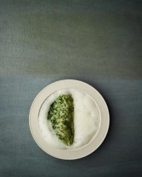 Overhead food photography of a grilled green vegetable wedge in white foam served on a plate by Ditte Isager.