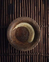 Top-down view of sliced vegetable in a textured earthenware bowl on a woven bamboo mat
