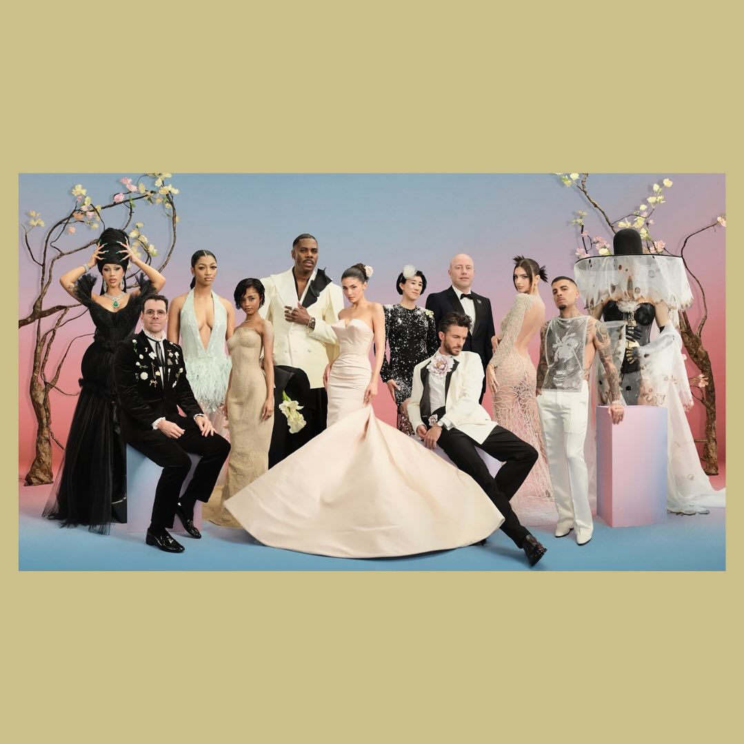 Group of diverse people in formal wear posing in front of floral background. Several are wearing wedding dresses and tuxedos.