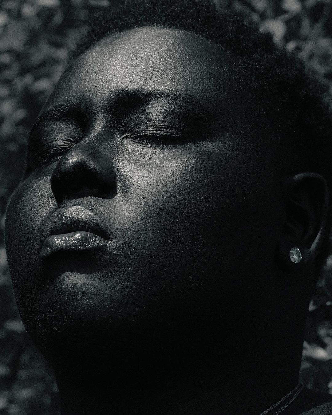 Close up portrait of a Black man with eyes closed outdoors against foliage