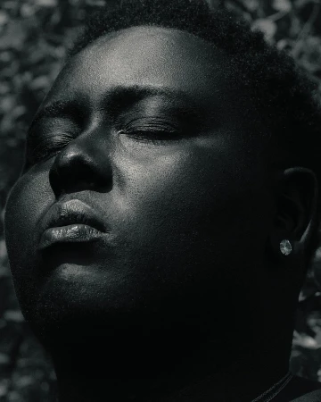 Close up portrait of a Black man with eyes closed outdoors against foliage