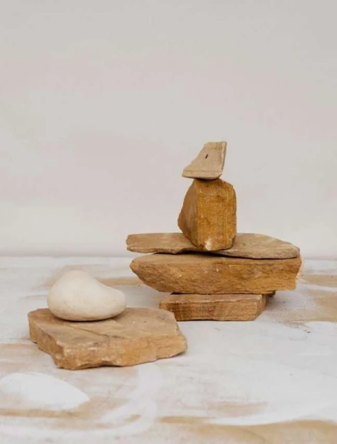 Stacked stones artfully arranged on textured surface, creating balance and natural sculpture in minimalist composition on neutral background.