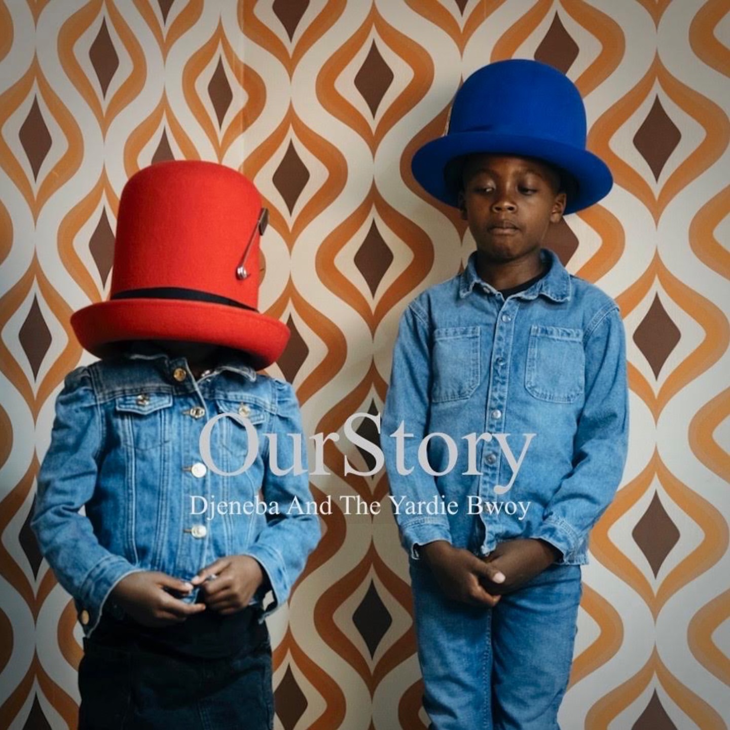 Two kids wearing oversized hats and denim jackets pose in front of a retro patterned wall. One wears a red hat, the other a blue hat.