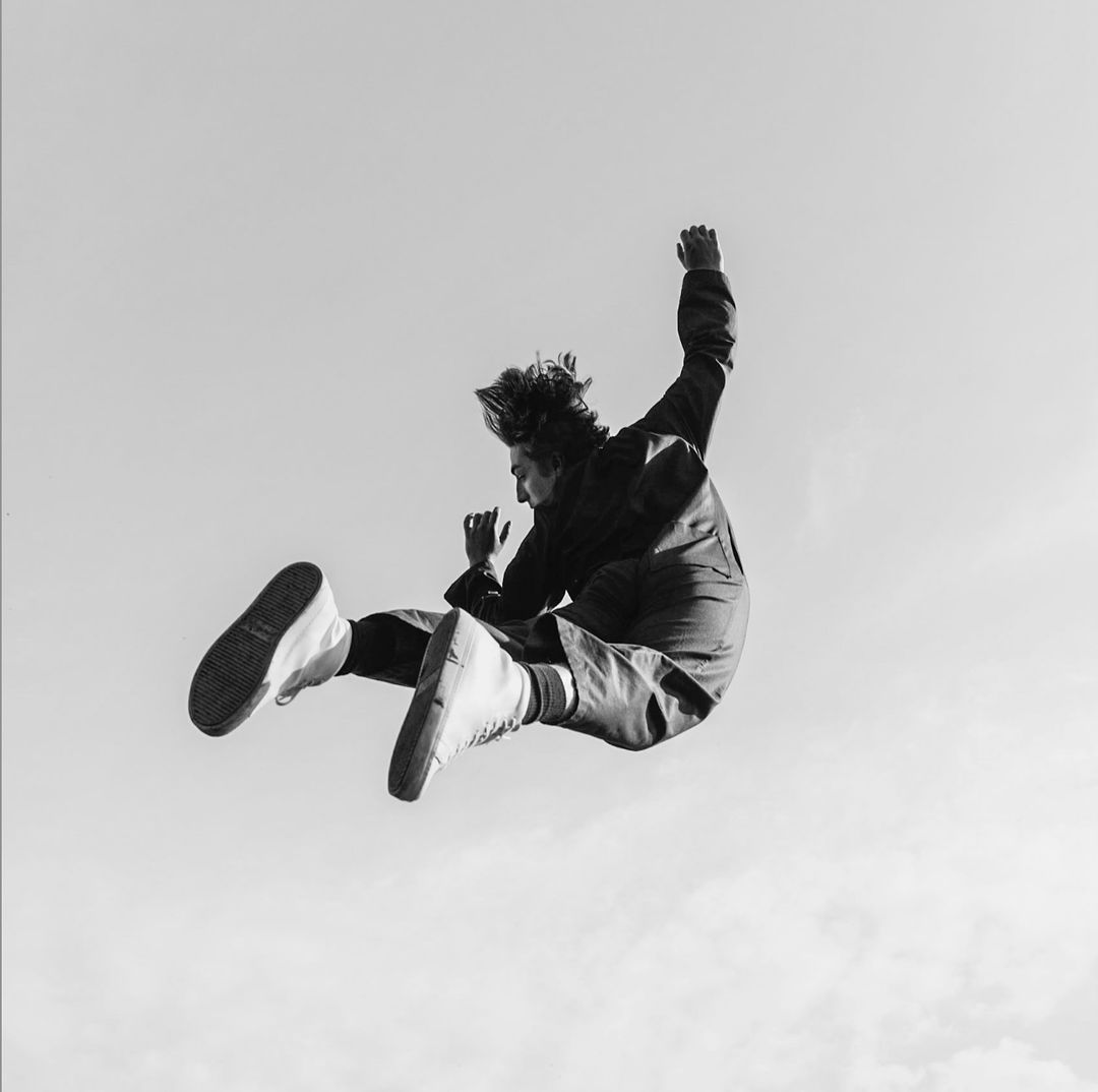 Black and white low angle shot of a person mid air jumping against a clear sky background
