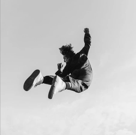 Black and white low angle shot of a person mid air jumping against a clear sky background