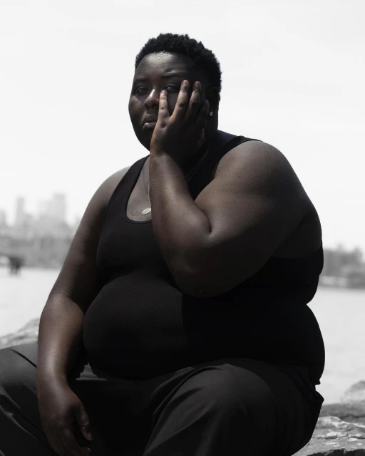 Monochromatic portrait of an African American adult female with short hair, hand to face, posing outdoors near a city skyline.