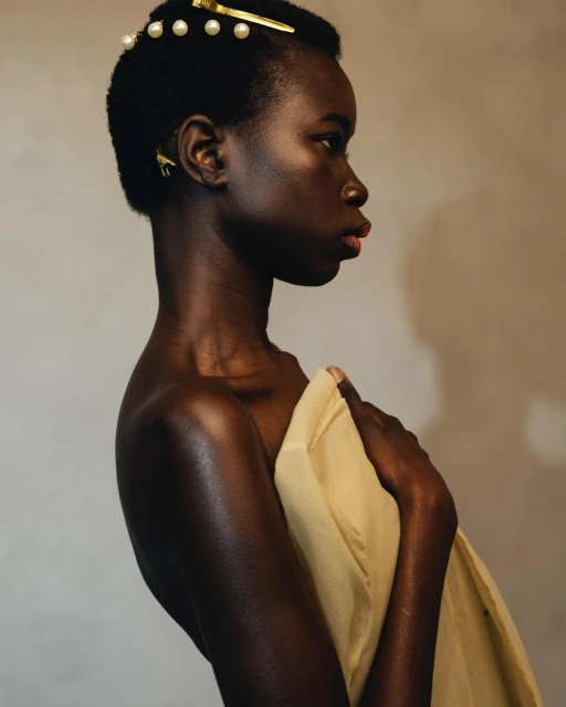 Profile view of an adult African female model with bare shoulders covered in fabric, posing in a photo studio with soft lighting.