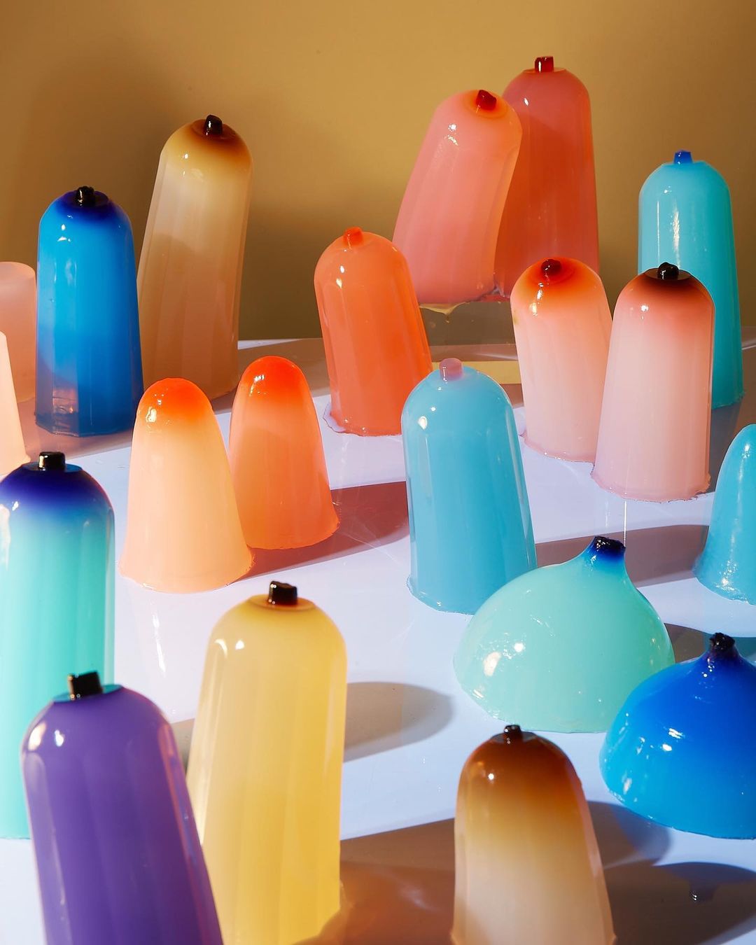 Array of colorful, translucent, minimalist bell-shaped objects with rounded tops, set on a white surface, creating a modern, abstract composition.