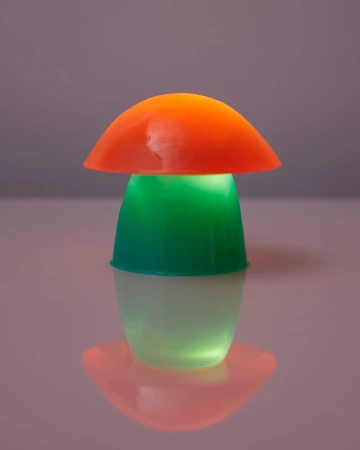 A mushroom-shaped lamp shines with orange, green, and white light, creating a colorful and playful illumination on a reflective surface.