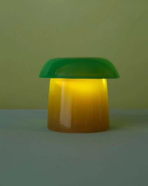 Illuminated green and yellow mushroom lamp casting a warm glow, set against a muted yellow background. Table lamp emitting light.