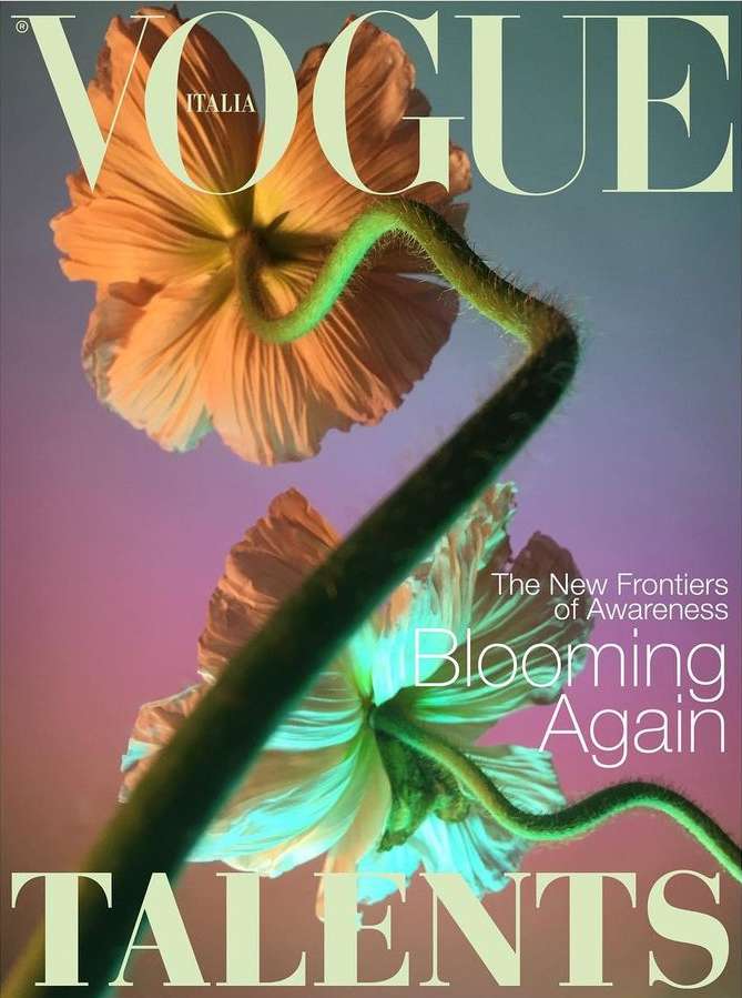 Vogue Italia magazine cover featuring a close-up of two peach-colored flowers with green stems on a muted blue and pink gradient background.