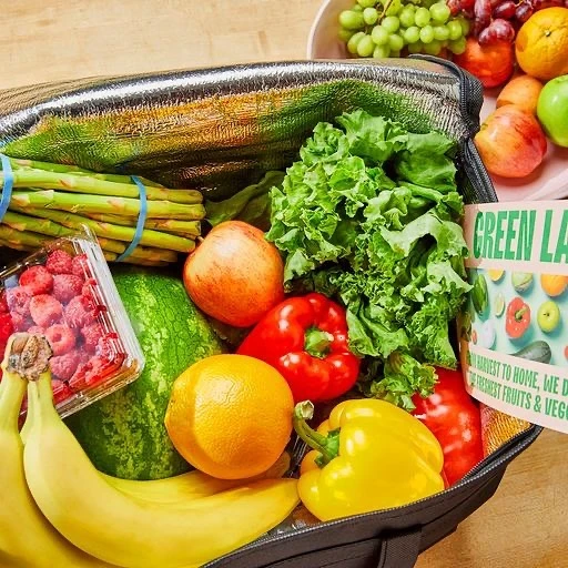 An insulated grocery bag is filled with fresh fruits and vegetables, including bananas, lettuce, peppers, oranges, and raspberries.