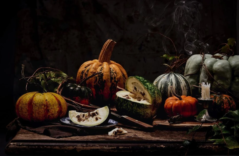 Still life with diverse pumpkins and gourds arranged on a wooden table with dark background, autumnal harvest display, smoke, and candle.
