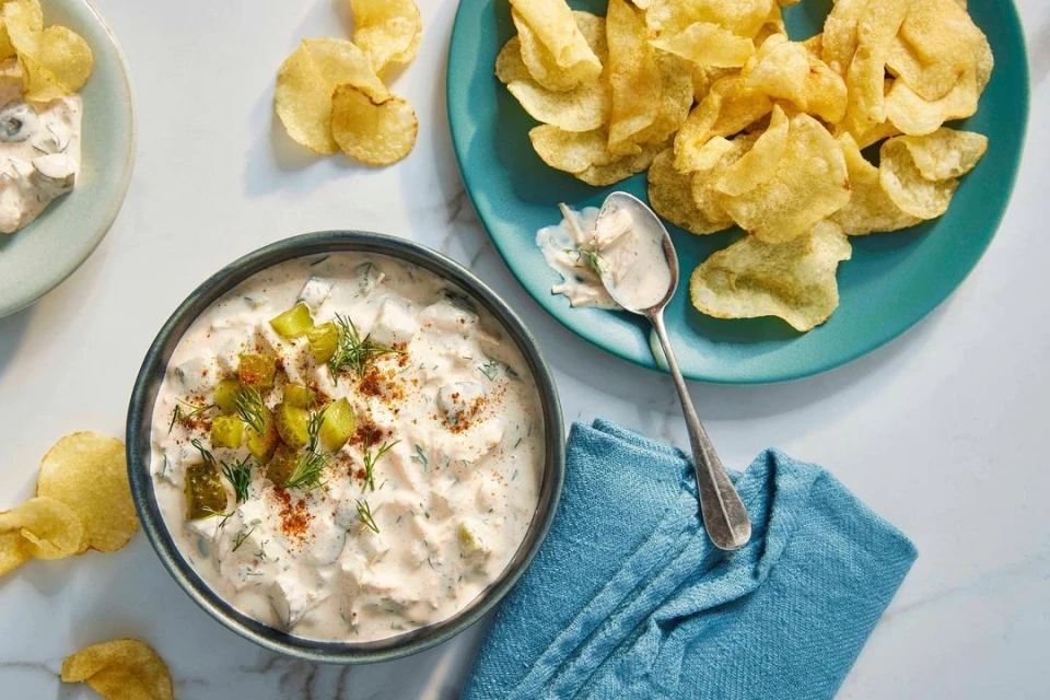 Overhead shot of dill pickle dip in a bowl with potato chips, showcasing a creamy dip with pickle pieces and fresh dill, ready to eat.