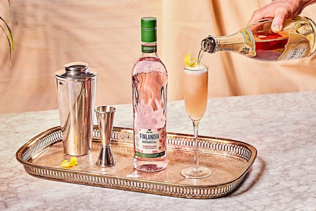 Champagne cocktail preparation with Finlandia Botanical drink, champagne bottle, cocktail shaker, and jigger on a decorative gold tray.